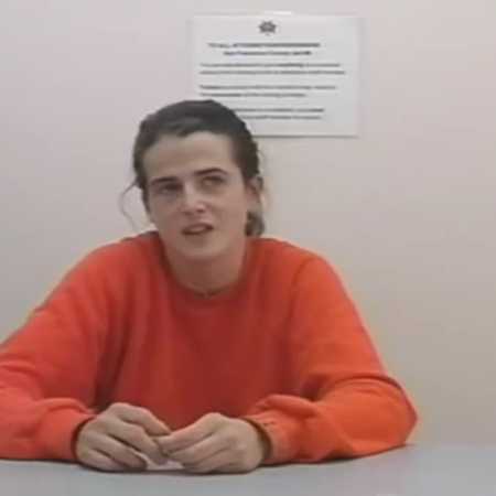 Woman sitting in orange shirt after being arrested 