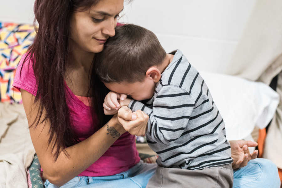 Son sits in mother's lap as he cries in their homeless shelter room