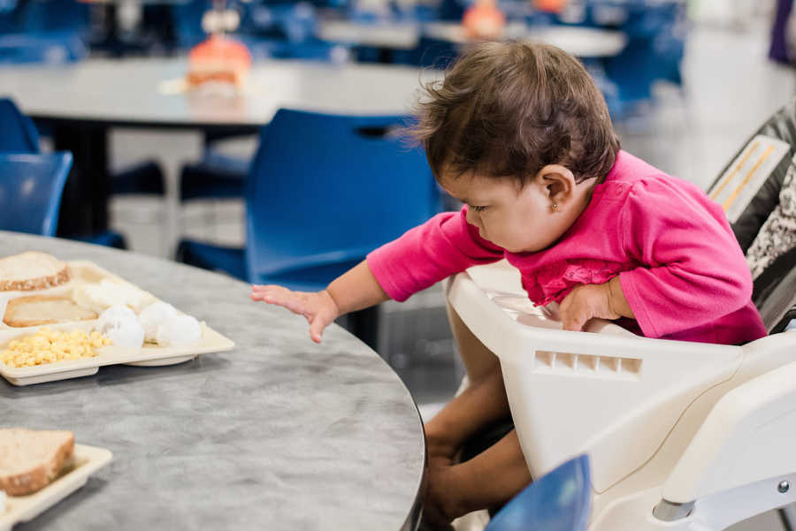 Baby girl in high chair reaching for food at homeless shelter