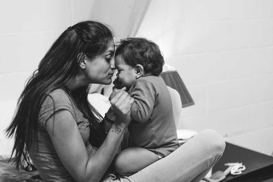 Mother sits with baby daughter in her lap forehead to forehead in homeless shelter