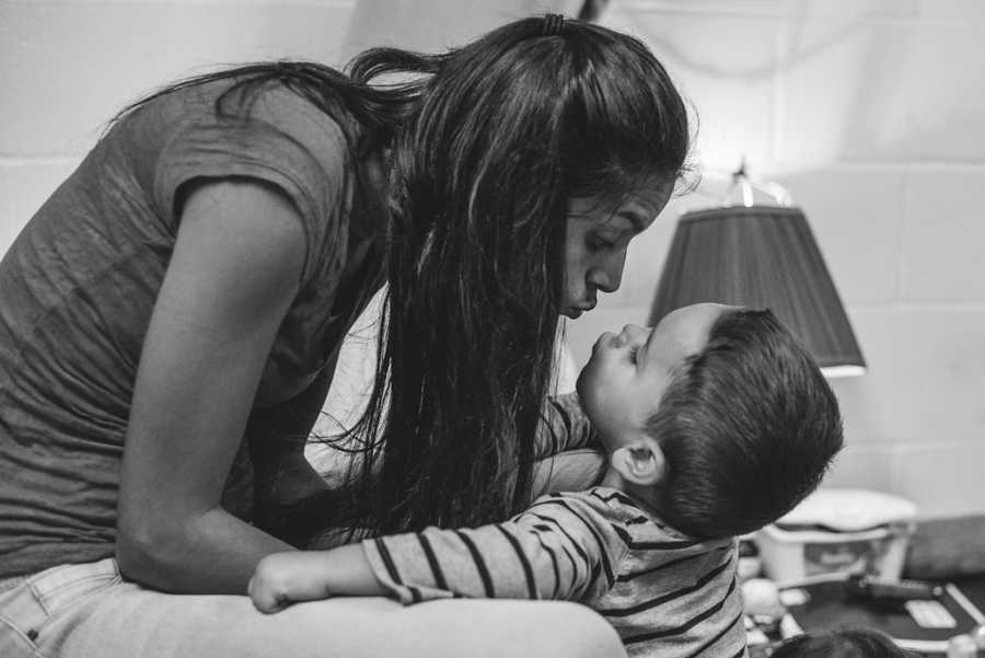 Mother leans over to kiss toddler on the lips in homeless shelter