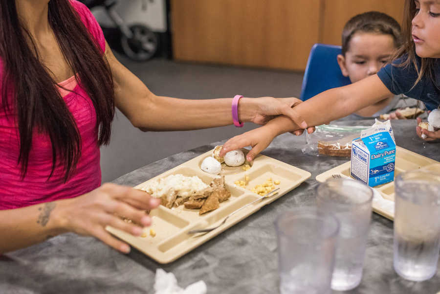 Daughter reaches across brother to grab food on mothers tray at homeless shelter