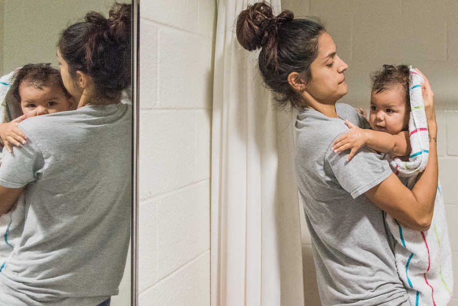Mother holds baby in towel who is looking over her shoulder at her reflection in mirror 