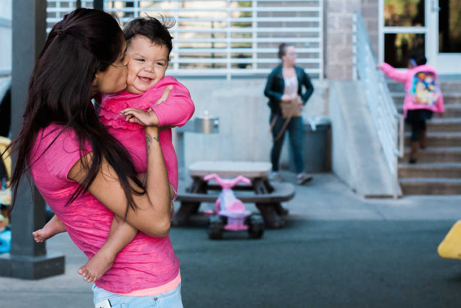 Mother holds daughter while giving her a kiss at homeless shelter