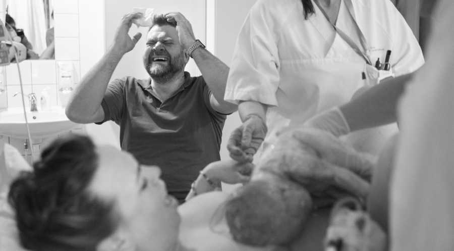 Husband crying hysterically with hands in air as wife gives birth