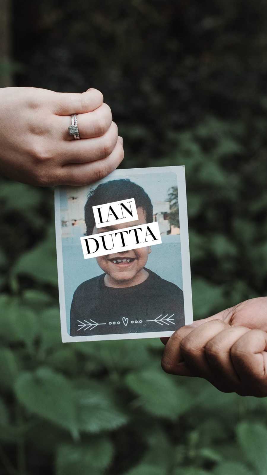 Close up of married woman's hand holding picture of little boy she will adopt with name, "Ian Dutta"