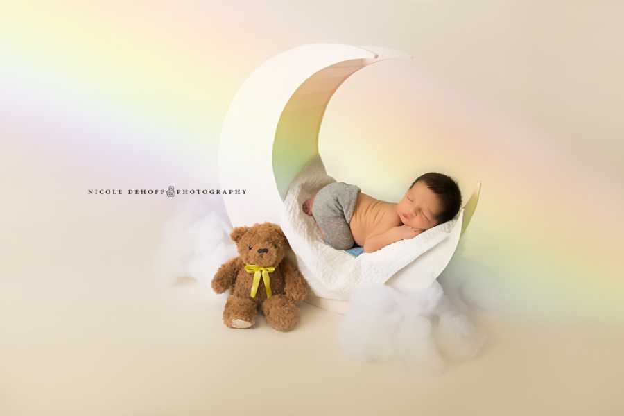 Newborn boy lays on moon structure with a teddy bear beside him