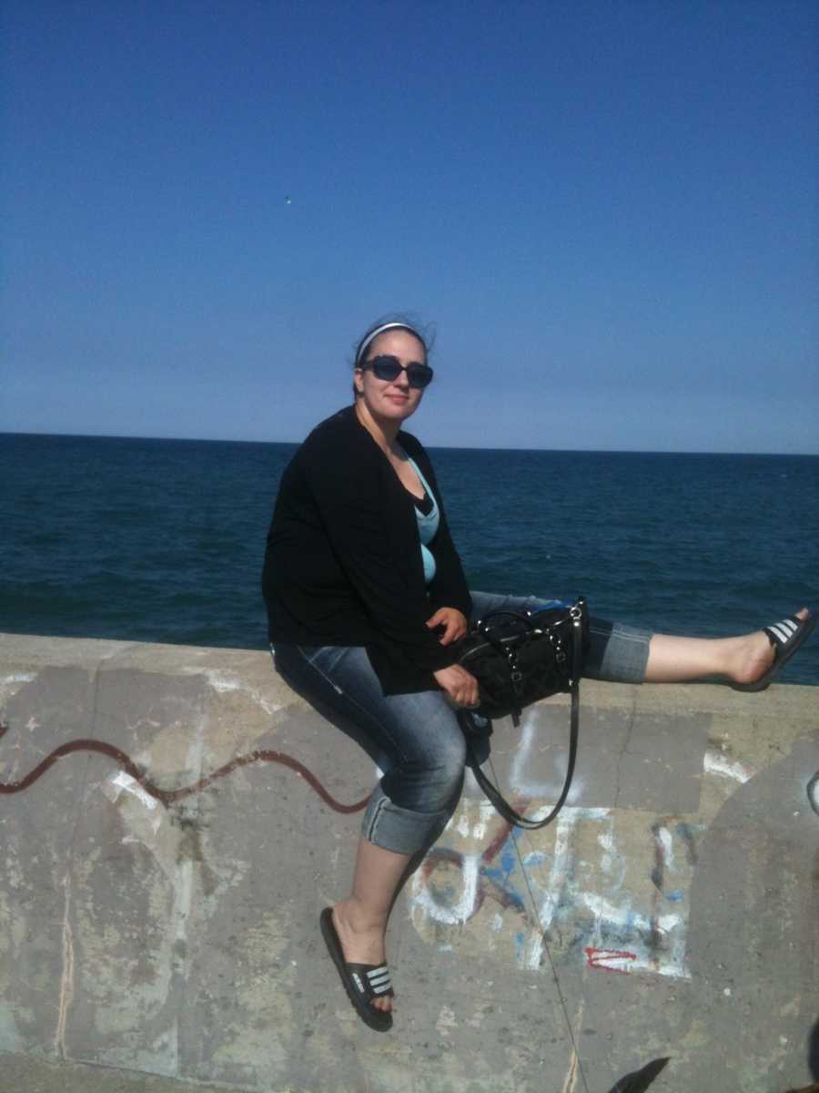 Woman who escaped her abuser smiling on cement wall with ocean in background