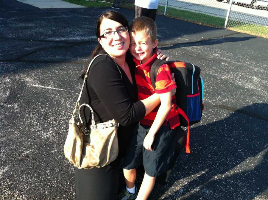 Woman who escaped her abuser kneels with toddler son who has backpack on