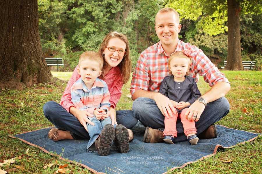 Husband and wife sit on blanket on grass with son and daughter with DIPG on their laps