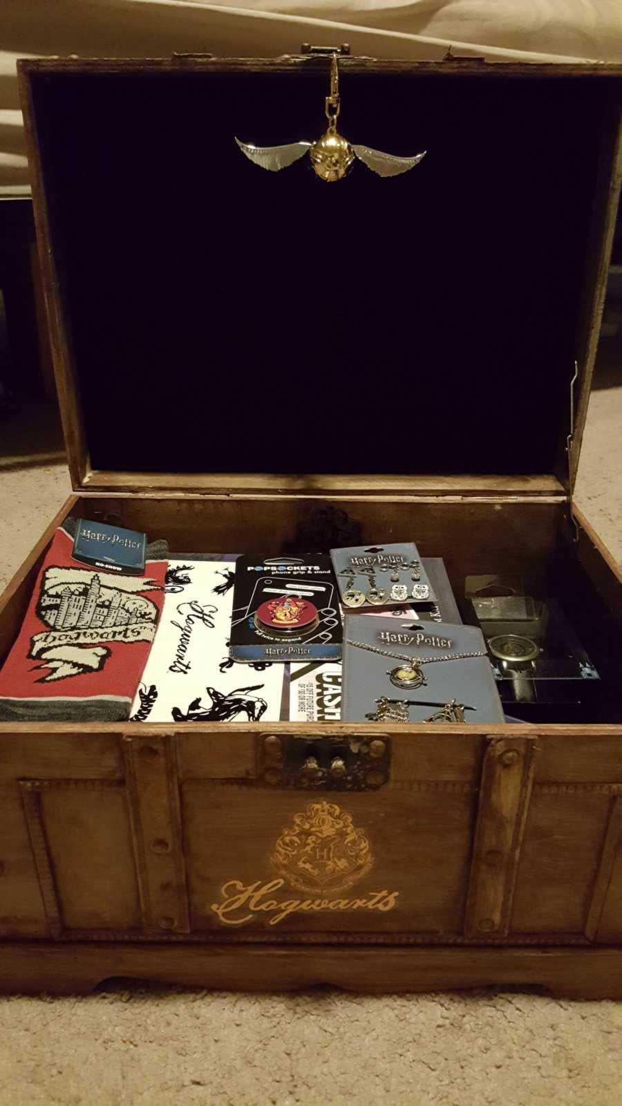 Trunk opened with golden snitch dangling from top of trunk with Harry Potter goodies inside 