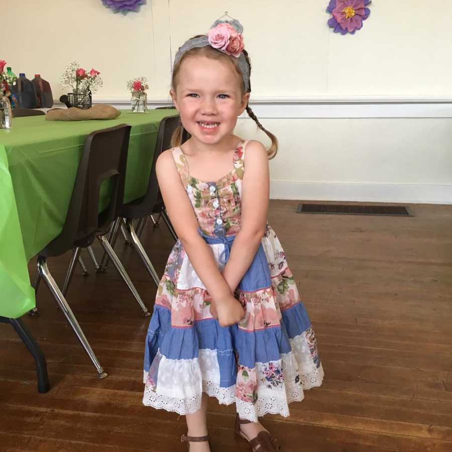 Little girl with DIPG and has since passed stands smiling in dress and flower headband