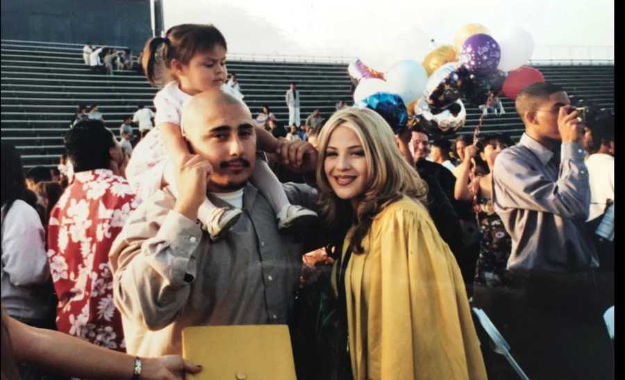 Teen parents at mother's high school graduation with daughter on father's shoulders