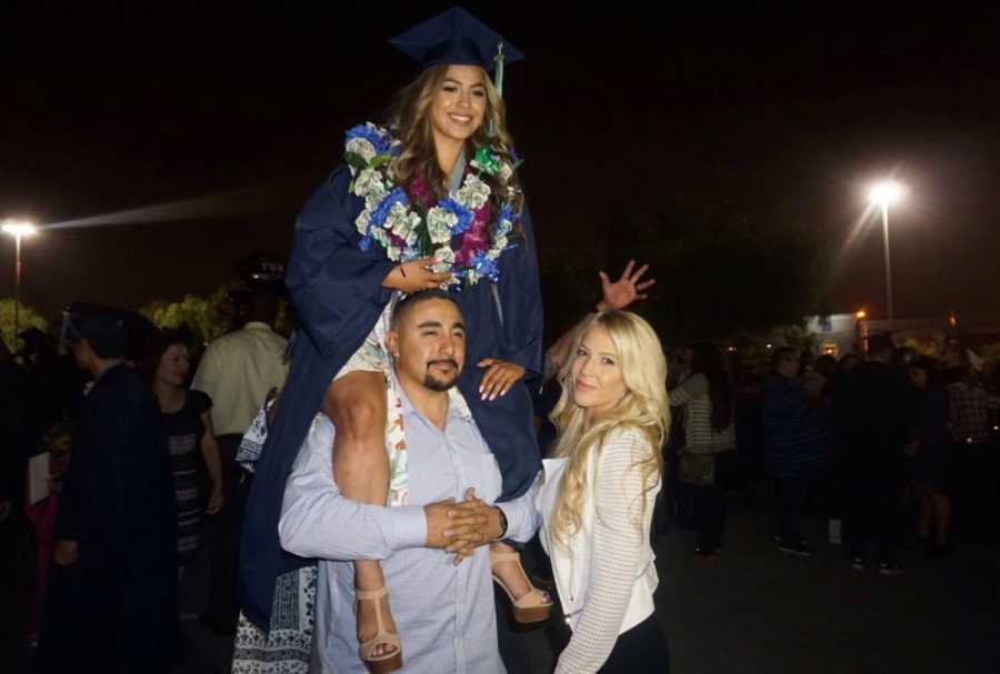 Daughter sits of fathers shoulders at her high school graduation with mother standing next to him