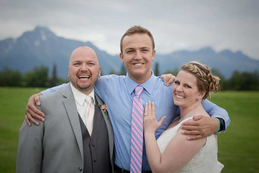 Bride and groom stand with man in the middle who has bride's late son's heart