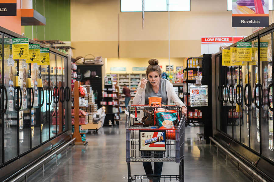Pregnant woman pushing shopping cart while eating a spoonful of ice cream