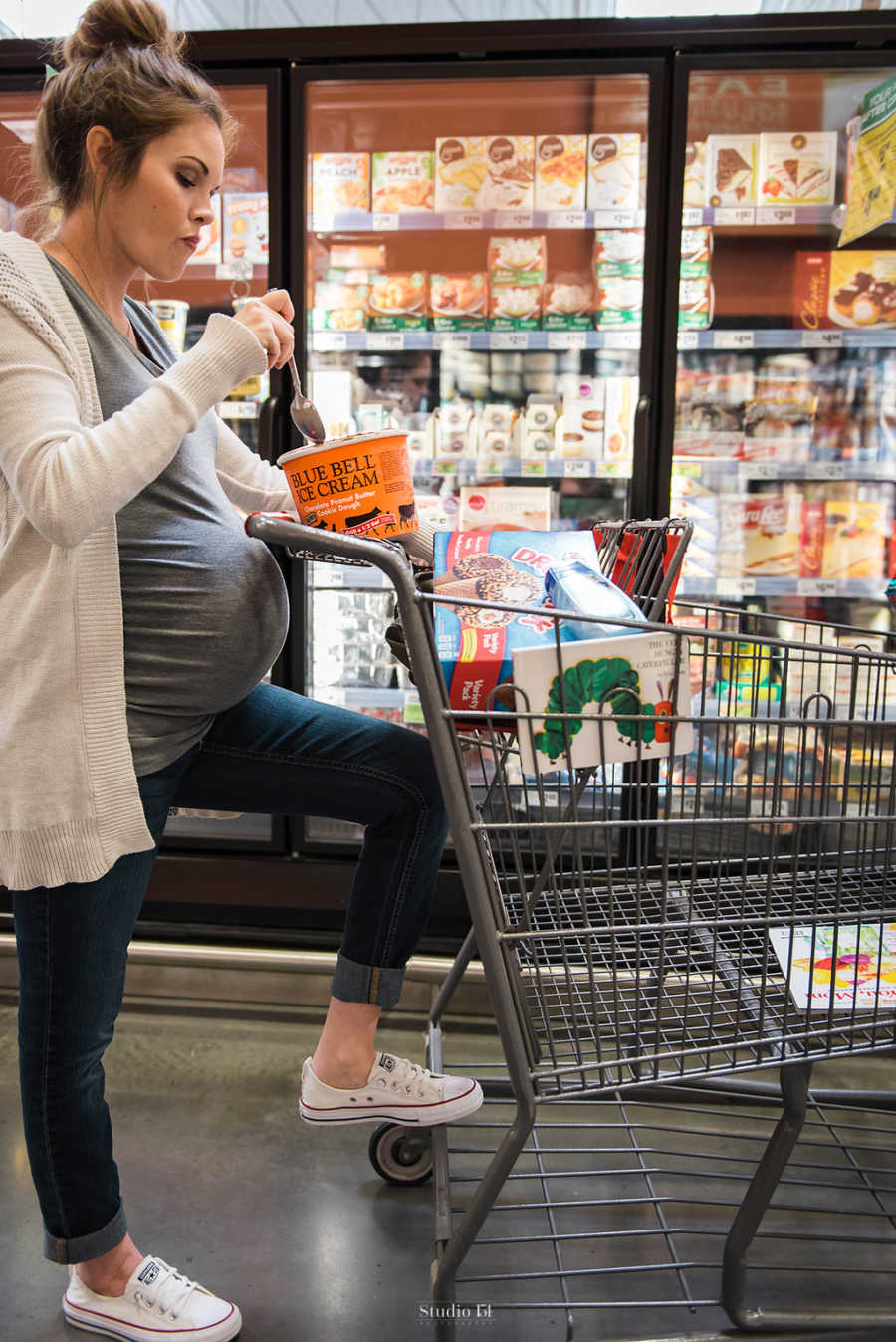 Side view of pregnant woman eating carton of ice cream in grocery store aisle