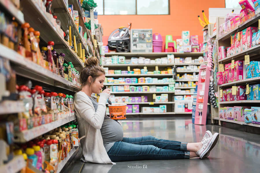 Pregnant woman sitting on floor of grocery store aisle eating carton of ice cream