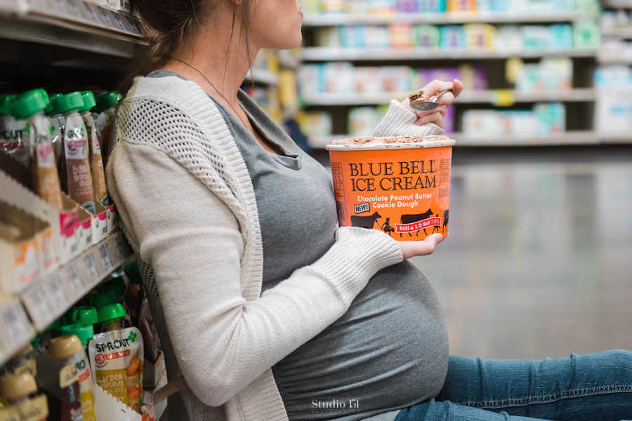 Close up of pregnant woman sitting on grocery store floor eating carton of ice cream