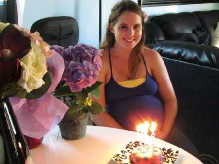 Pregnant 19 year old sitting at table with flowers and cake with candles on it