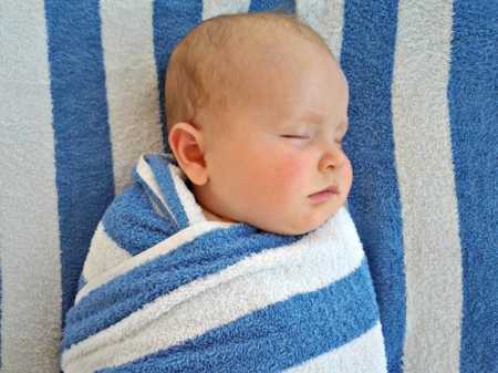 Infant asleep swaddled in blue and white striped towel whose mother is reminded that raising little ones is magical