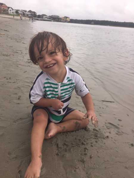 Toddler with mild cerebral palsy due to hemiplegia smiling while playing in sand at beach