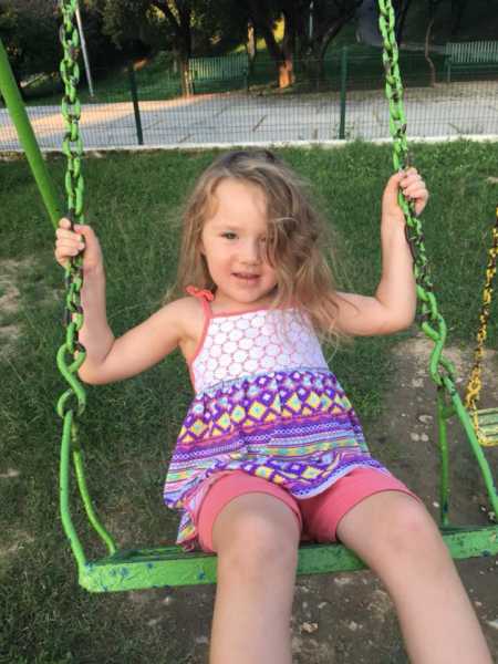 Two year old with DIPG smiles as she swings on swing set 