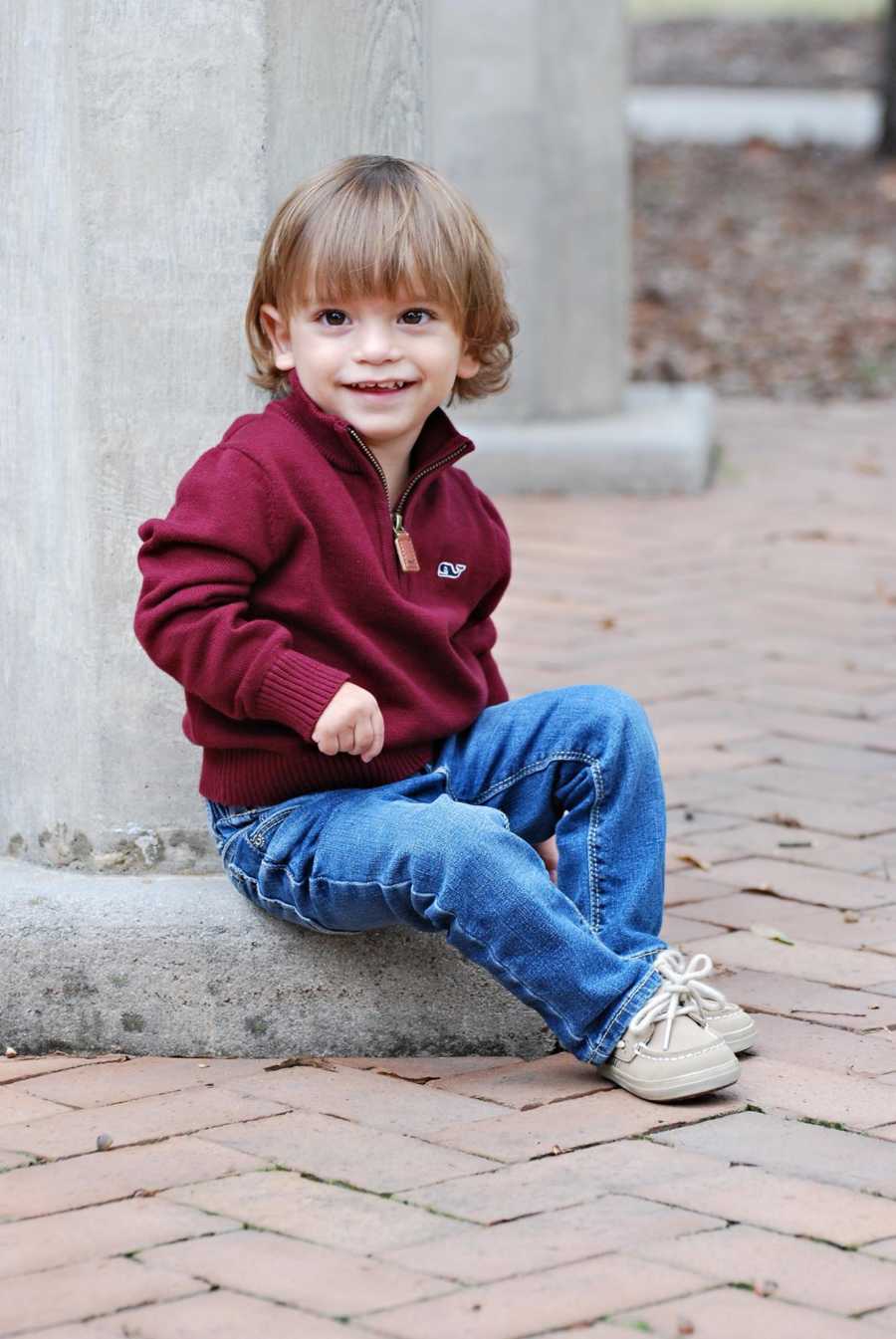 Toddler with mild cerebral palsy due to hemiplegia sitting on cement post smiling