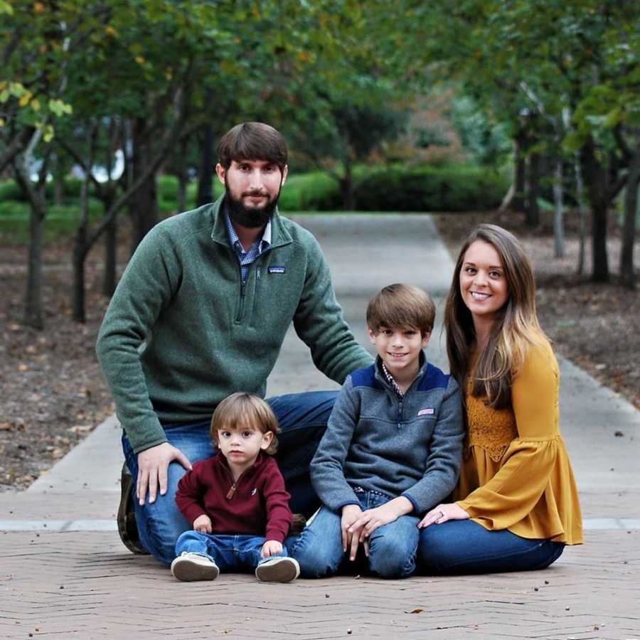 Mother and father sit on ground with their oldest son and son with mild cerebral palsy due to hemiplegia