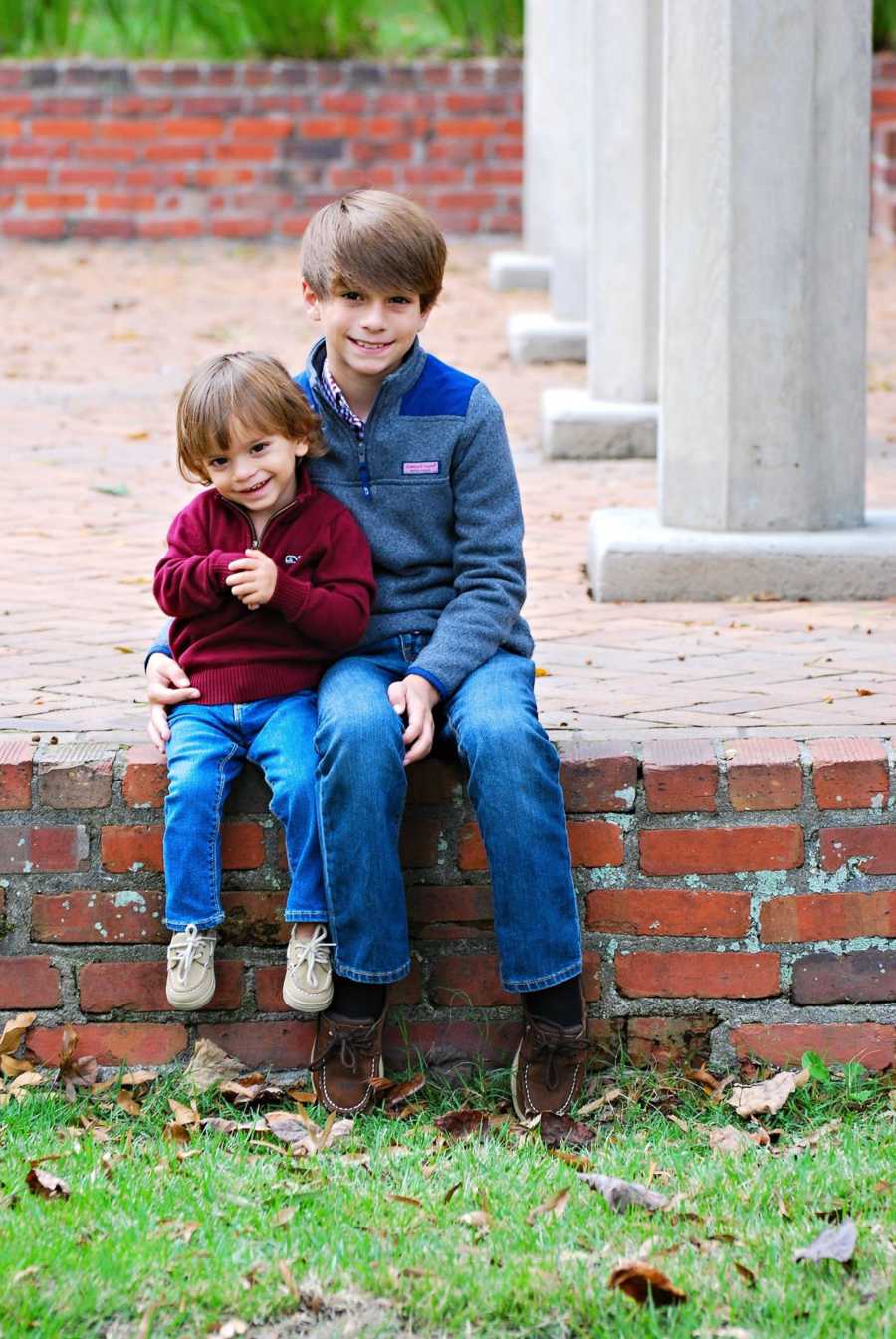 Toddler with mild cerebral palsy due to hemiplegia sitting next to older brother