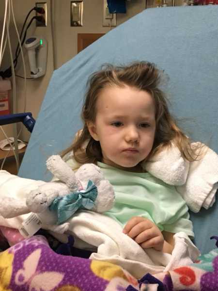 Two year old little girl with DIPG sitting in hospital bed with stuffed animal