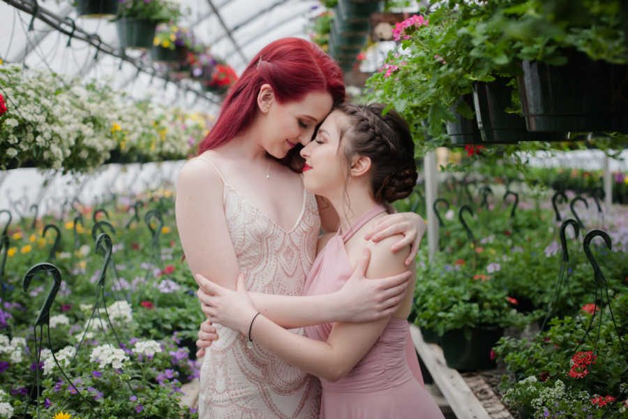 Girlfriends hold each other close in flower nursery