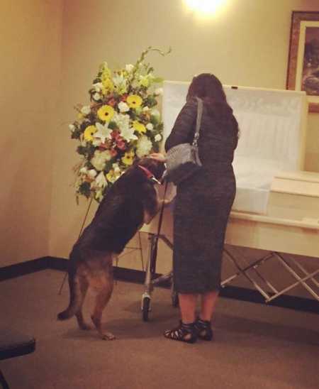 Wife looks at open casket of her husband with dog