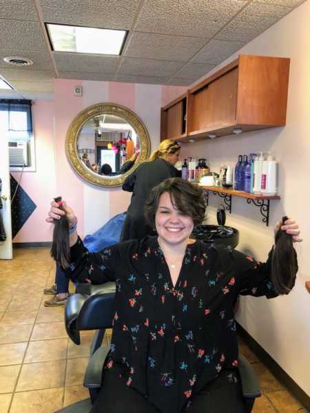 21 year old sits in salon chair holding hair she is donating to Pantene for cancer patient