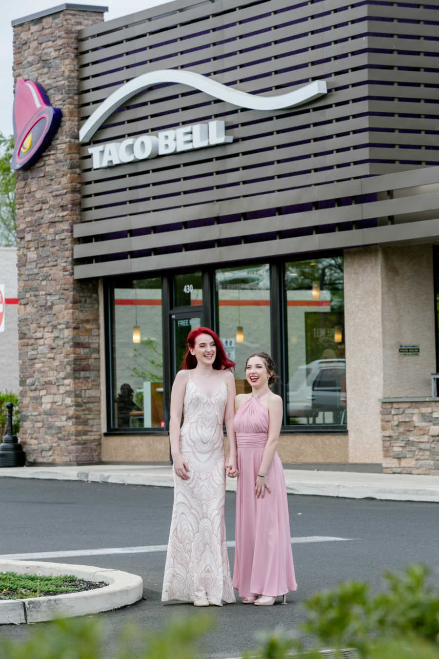 Girlfriends stand in Taco Bell parking lot in prom dresses
