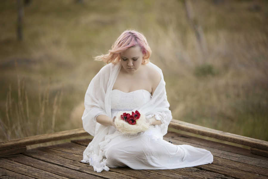 Woman who has Diminished Ovarian Reserve sits in all white holding pile of red roses