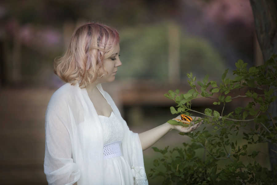 Woman with Diminished Ovarian Reserve stands holding branch of plant with butterfly on it