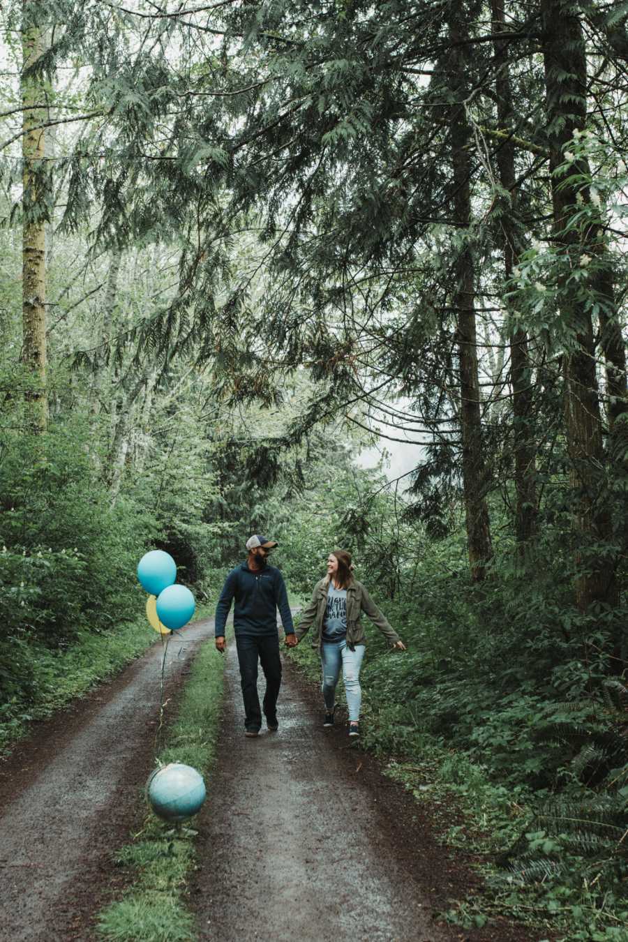 Husband and wife who are adopting a child from India, walk in path in forest with blue balloons