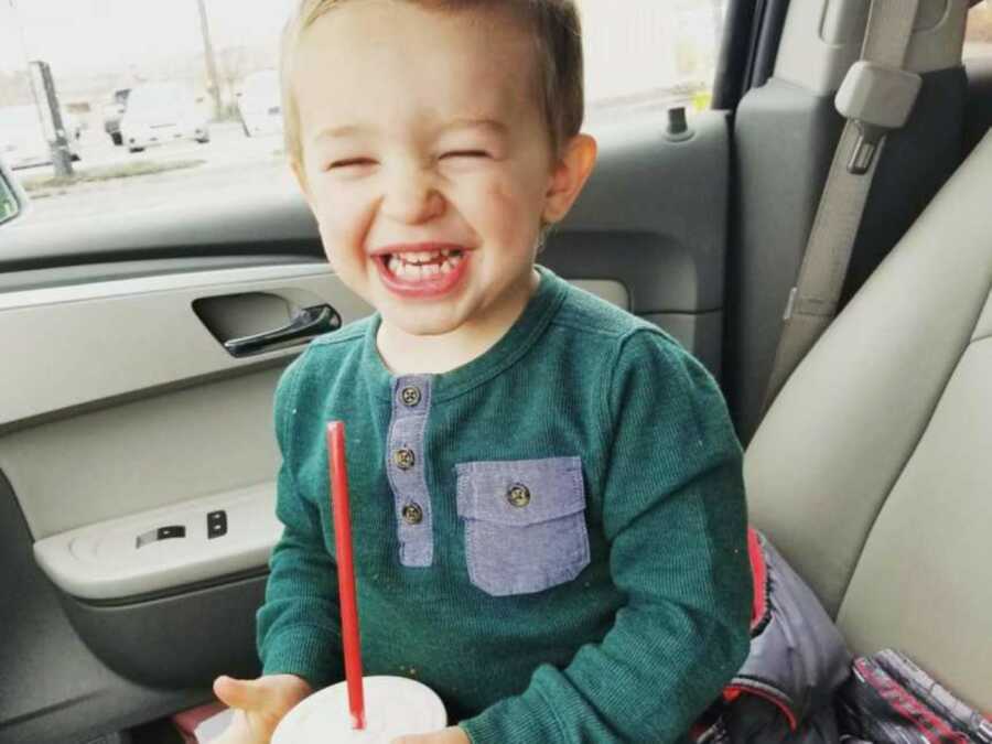 Little boy smiles big while sitting in the car and drinking a smoothie out of a red straw