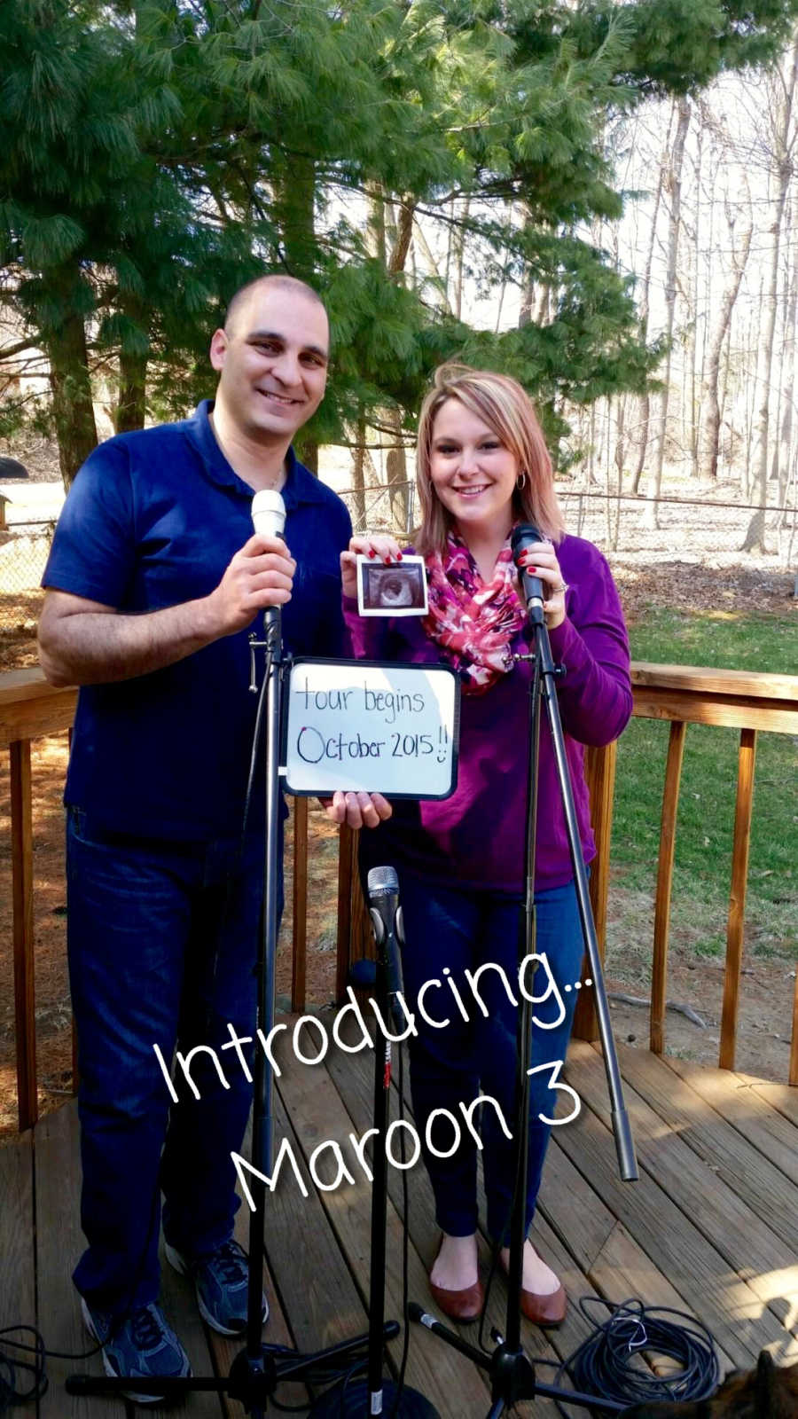 Husband and wife standing holding ultrasound in front of microphones holding sign saying, "tour begins October 2015"