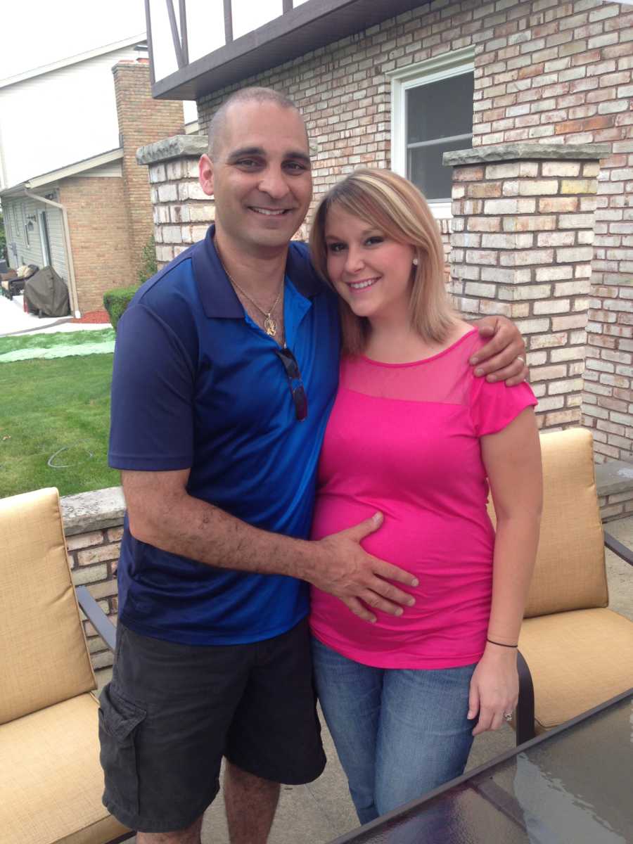 Husband stands with arm wrapped around pregnant wife and hand on her stomach