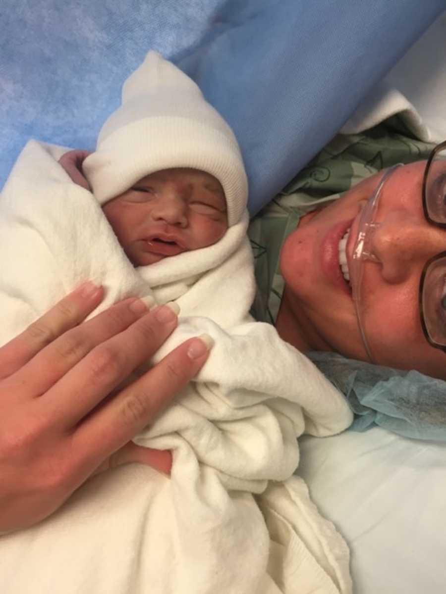 Mother smiles with newborn sleeping on her chest who had pediatric stroke in womb