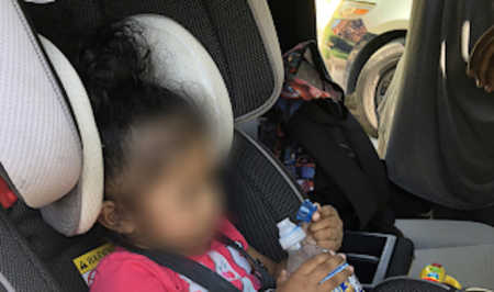 Blurred out face of baby who was sitting in hot car for hours but saved by officer holding water bottle
