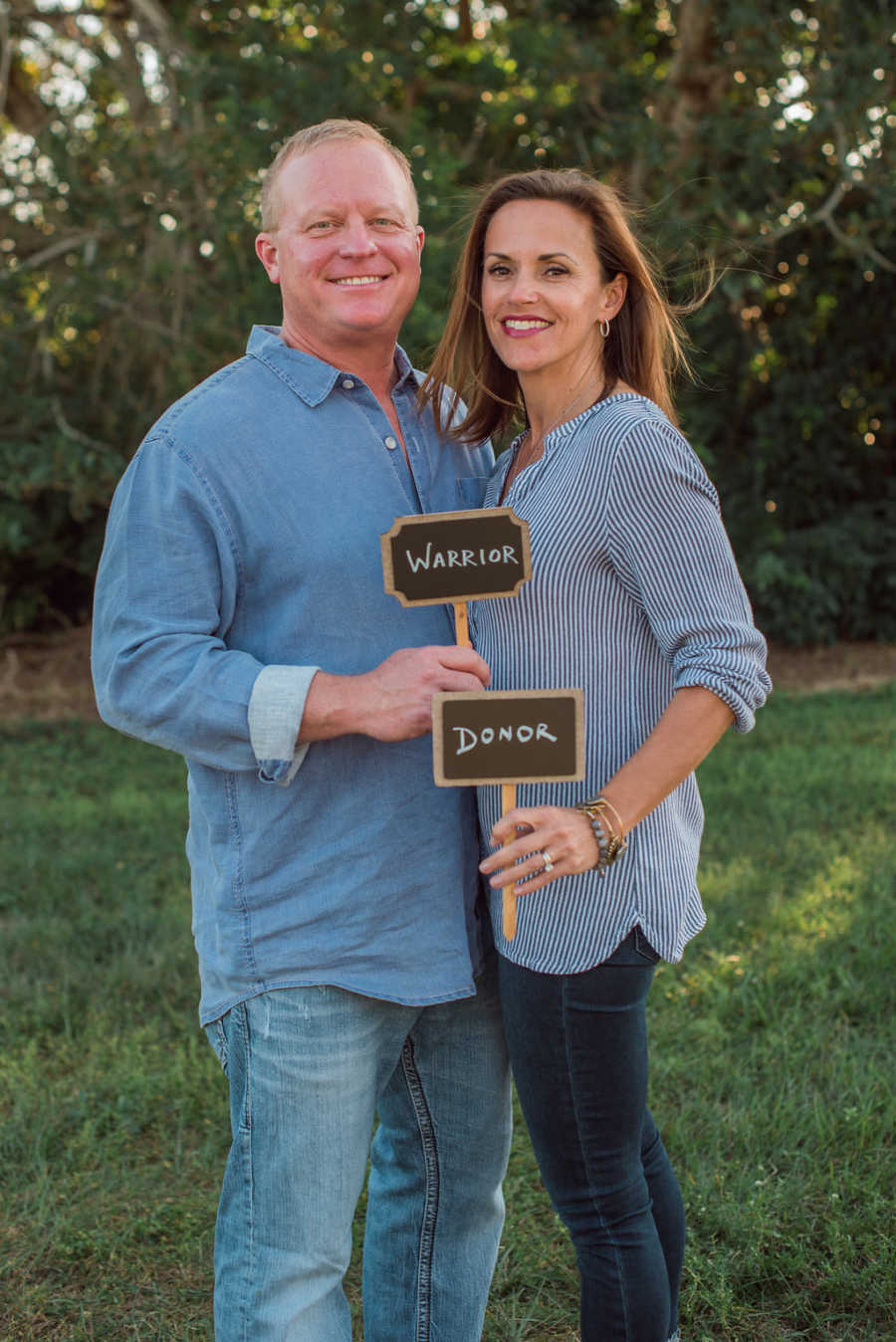 Woman who donated kidney to friend's husband stands holding sign saying, "donor" next to her husband 