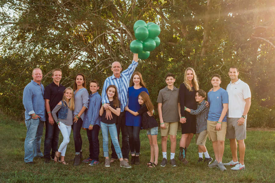 Man who had kidney transplant stands with family holding green balloons beside donor and family and another family