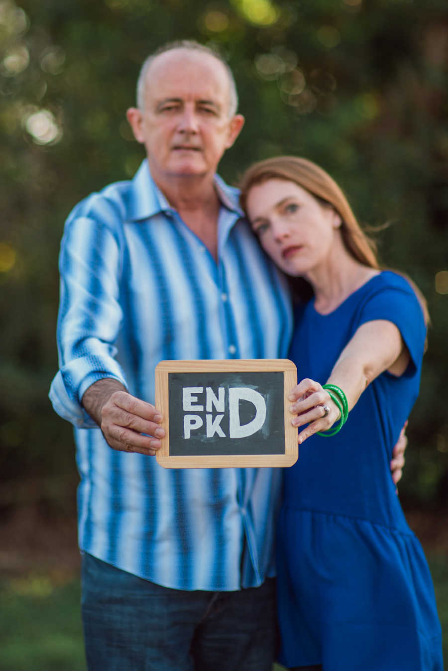 Wife and husband who need kidney transplant stand arm in arm holding sign with letters E,N,P,K and D