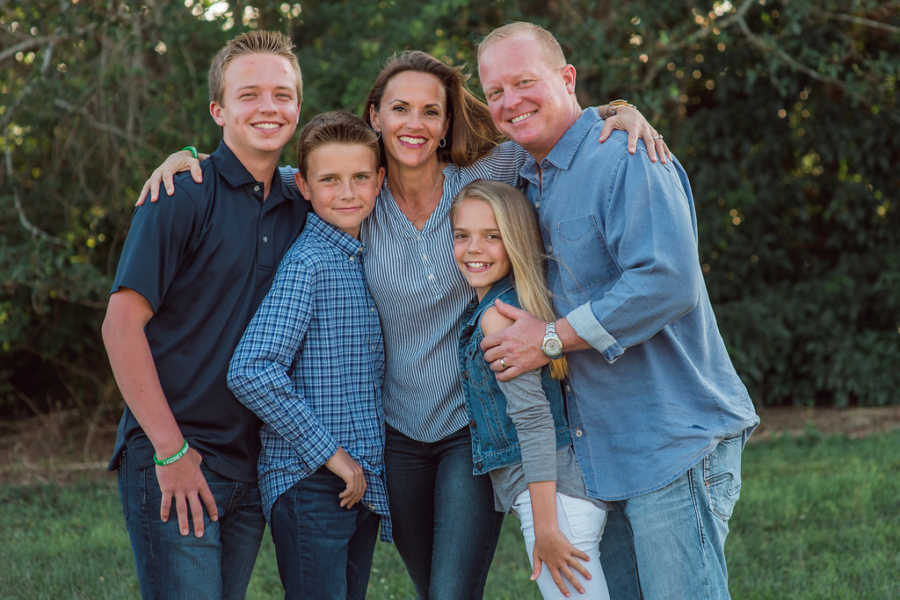 Woman who donated kidney to friend's husband stands smiling with husband, daughter, and two sons