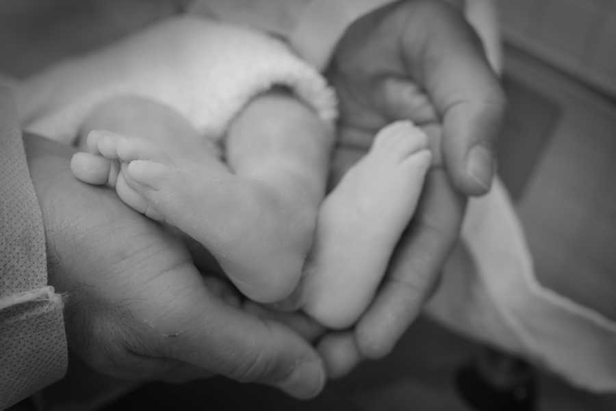 Mother holds stillborn baby's feet in her hands
