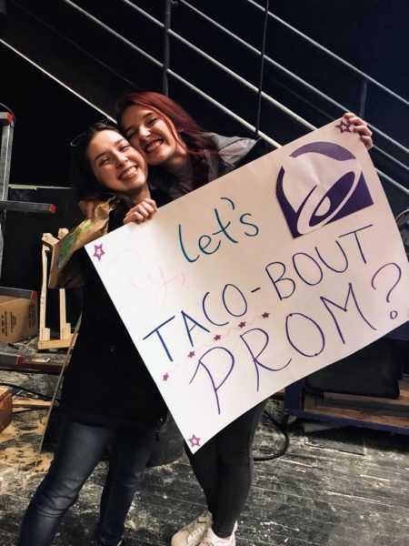 Girlfriends stand holding prom-posal poster that says, "let's taco-bout prom"