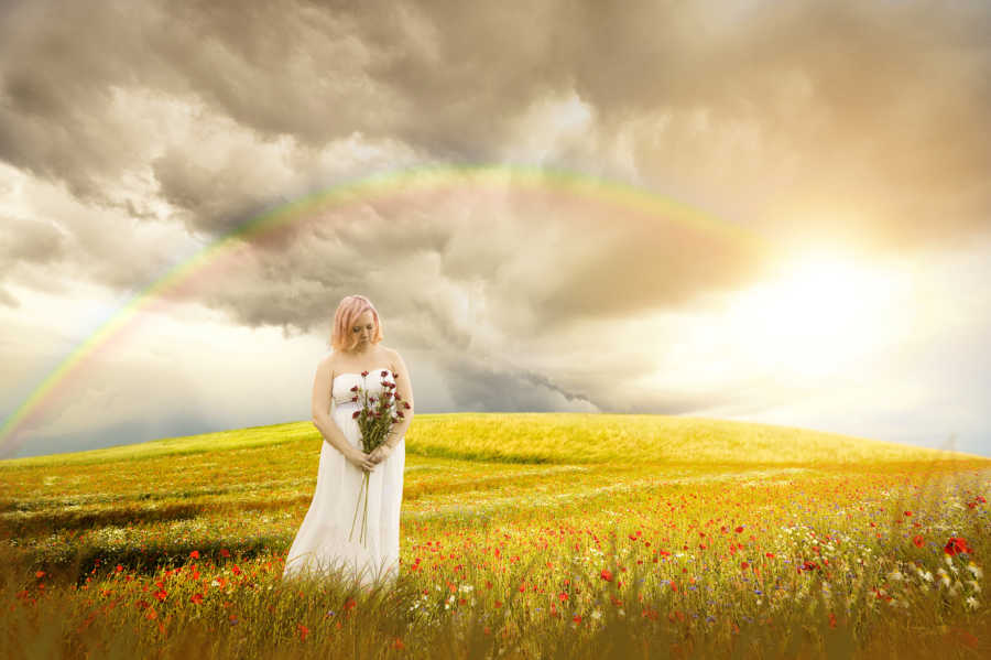 Woman with Diminished Ovarian Reserve stands in field holding flowers with rainbow in background